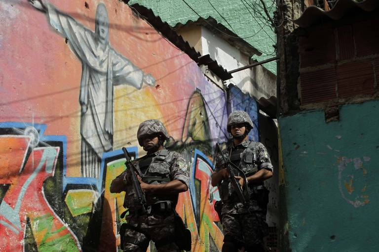 Policiais da Força Nacional caminha em frente a grafite do Cristo Redentor no morro Santo Amaro, no Rio de Janeiro
