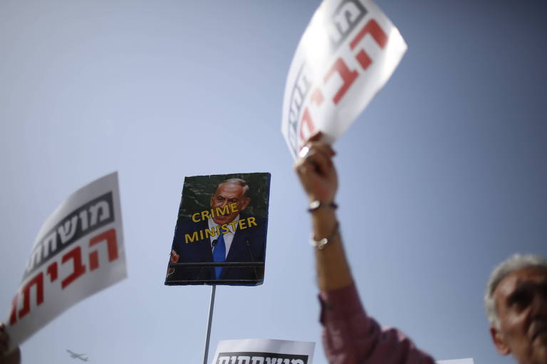 Manifestante carrega cartaz com mensagem "Ministro do Crime" em protesto contra o premiê israelense, Binyamin Netanyahu, em Tel Aviv
