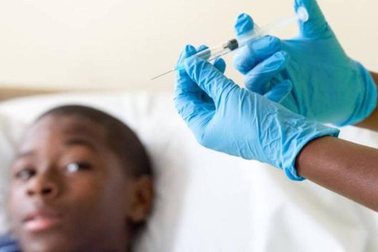 Profissional de saúde prepara injeção para aplicação em criança, que observa o processo