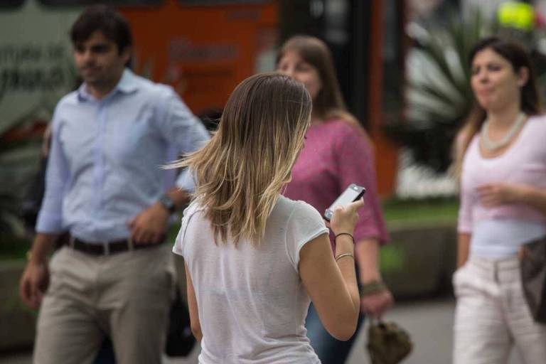 Mulher caminha enquanto olha o celular.