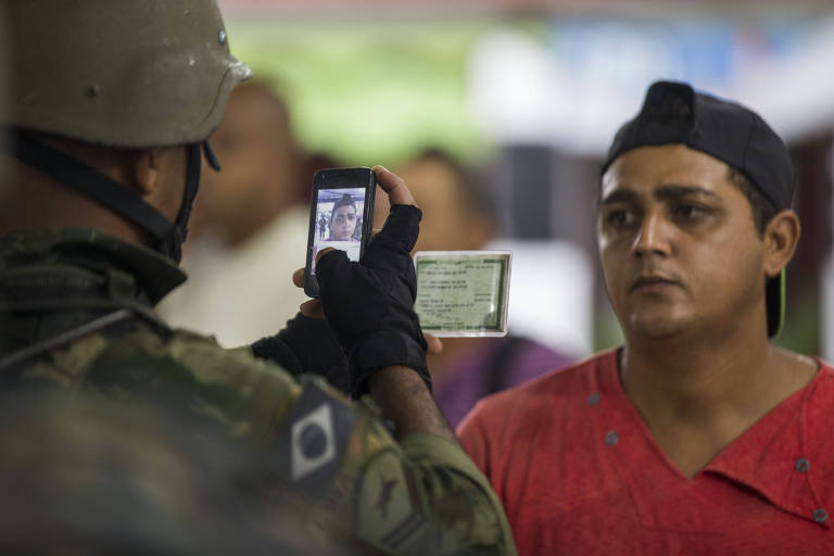 Homem das Forças Armadas tira foto de morador em comunidade ocupada do Rio