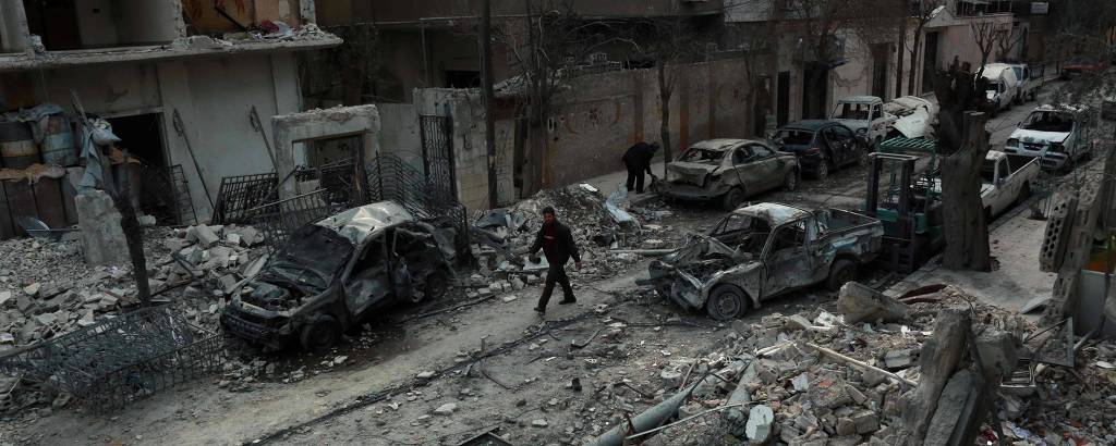 Homem caminha próximo a prédios destruídos após ataques aéreos do governo sírio na região de Douma