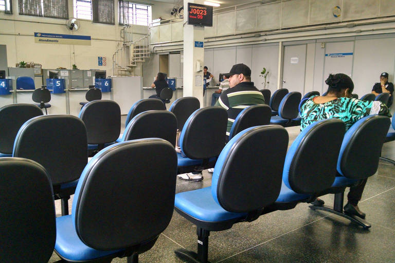 Cadeiras vazias e duas pessoas aguardando em posto do INSS