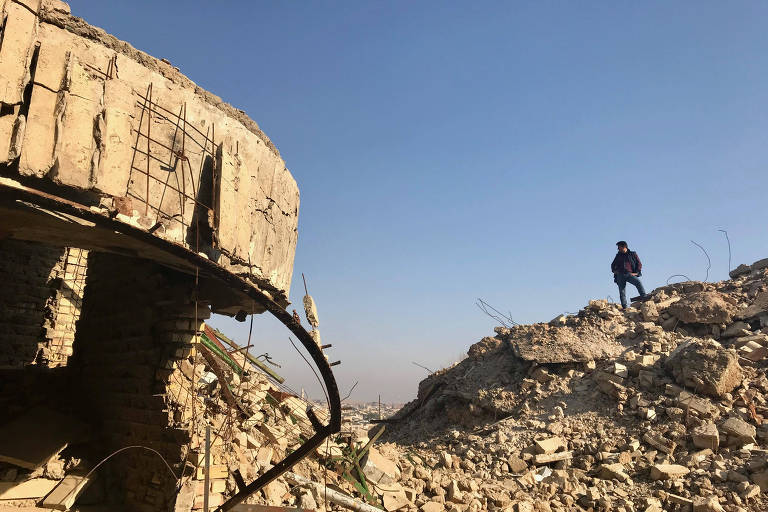 Do alto de uma pilha de entulho, homem mostra o que sobrou da mesquita de Jonas, um dos prédios históricos de Mossul destruídos pelo Estado Islâmico