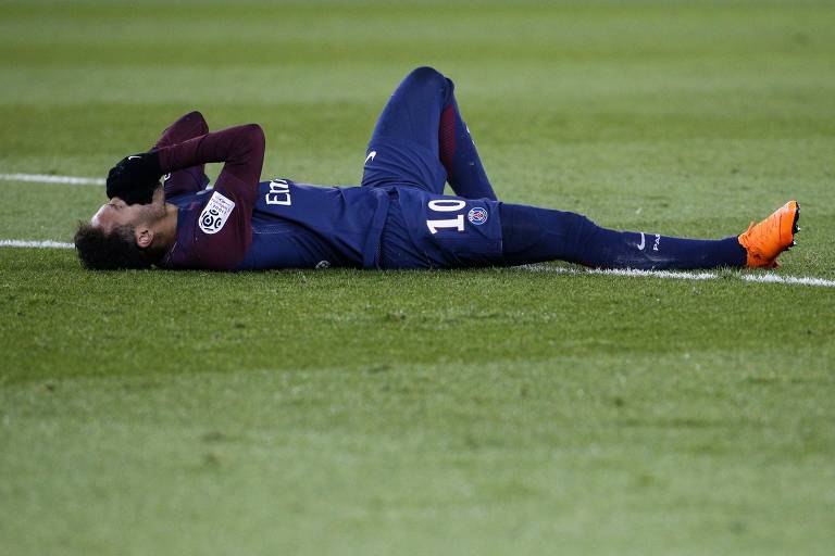 Deitado no gramado com a camisa do PSG, o brasileiro Neymar chora após torcer o pé