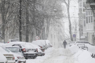 A man walks past cars parked along a snow-covered street as snow falls in central Kiev