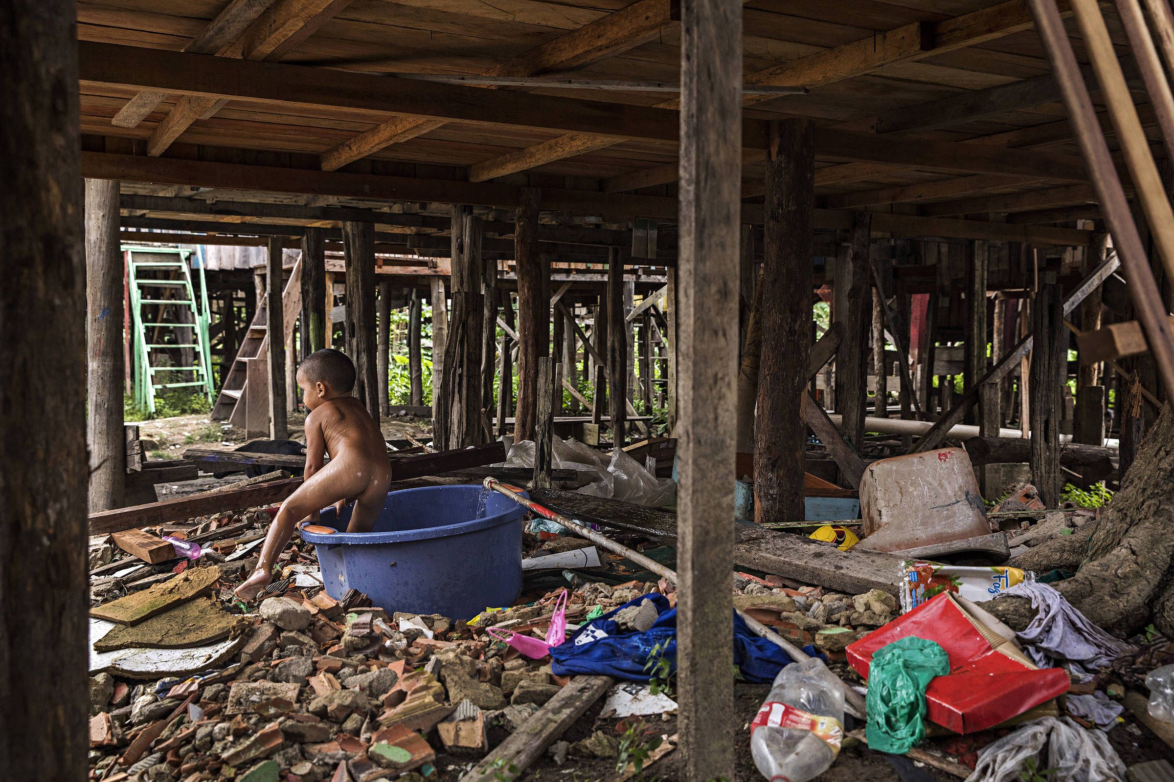 Garoto de três anos toma banho em bacia em meio a lixo acumulado em favela de palafita atingida por enchentes em Manaus