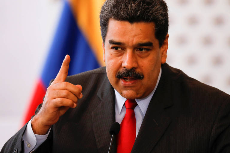 Nicolás Maduro, de terno preto e gravata vermelha e com a bandeira da Venezuela ao fundo, fala e gesticula com a mão direita