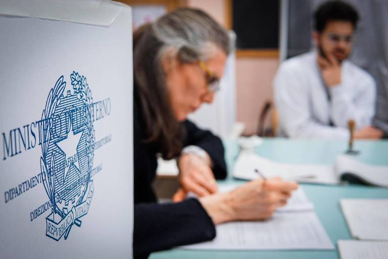 Com urna em primeiro plano, foto mostra mulher contando votos da eleição italiana em Nápoles, no sul do país