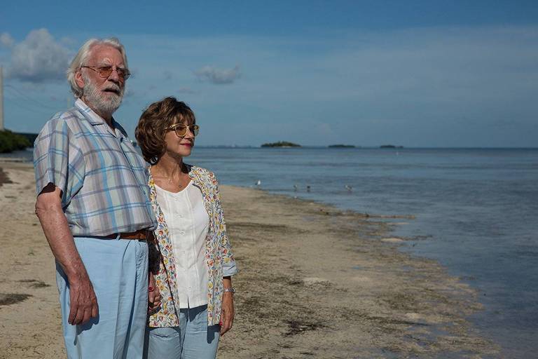 Donald Sutherland e Helen Mirren estão caracterizados como seus personagens John e Ella, de pé numa praia, usando roupas esportivas, mas não de banho, olhando o mar, no filme "Ella e John", do italiano Paolo Virzì