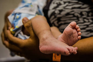 Mãe segura filho com microcefalia no colo no Recife