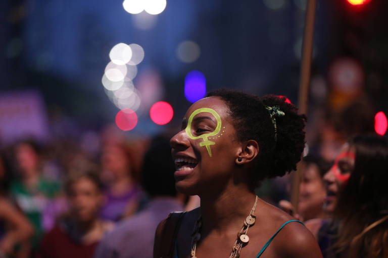 Garota com o símbolo do feminino pintado no rosto durante Marcha das Mulheres