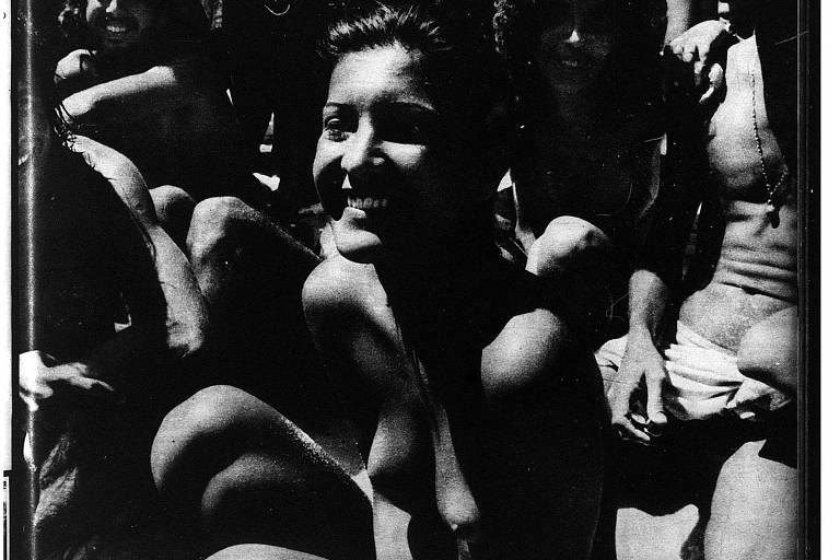 Foto em branco e preto mostra moça que fez o primeiro topless do Brasil, em 1972; ela tem os cabelos molhados para trás e está em meio a um grupo de banhistas de Ipanema, retratado em plano vertical, bem fechado
