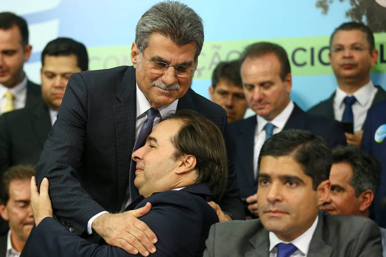 O senador Romero Jucá (MDB-RR) abraça Rodrigo Maia (DEM-RJ) (sentado) durante convenção do DEM que alçou ACM Neto à presidência do partido e lançou a pré-candidatura de Maia à Presidência da República