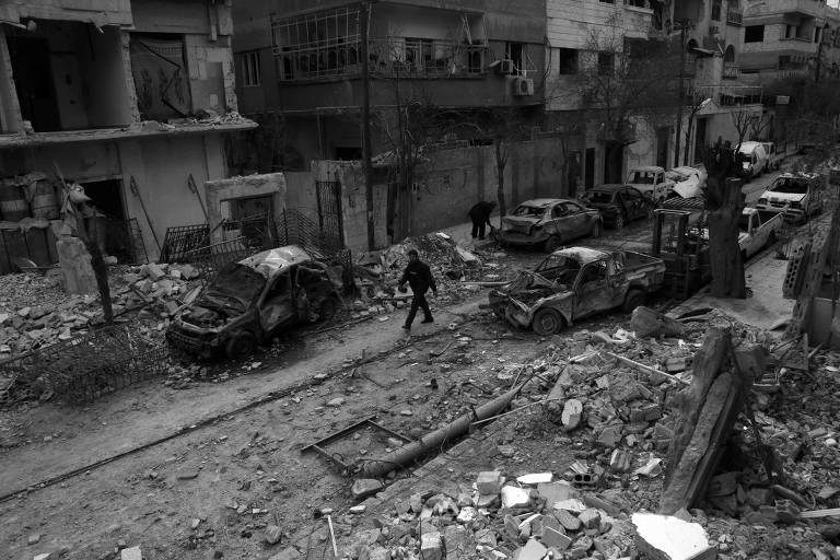 Homem caminha em meio a imóveis e veículos atingidos por bombardeios, em Douma, na Síria
