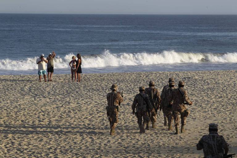 Soldados em uma praia com turistas ao fundo