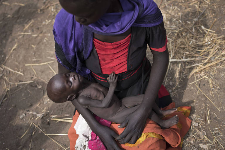 Mãe espera com filho de dez meses no colo em fila para distribuição de comida em Malualkuel, no norte do Sudão do Sul