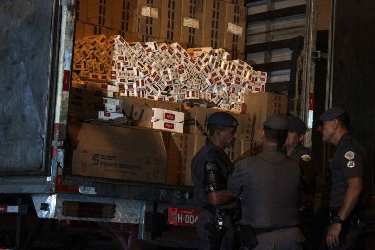 Policiais militares conversam ao lado da traseira de um caminhão com cigarros contrabandeados, vindos do Paraguai