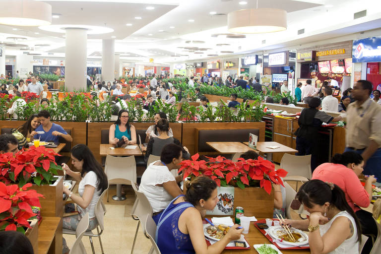 Pessoas sentadas fazem refeição em mesas de praça de alimentação de shopping