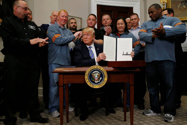 O presidente Donald Trump mostra documento com assinatura da sobretaxa ao aço importado, rodeado por funcionários da indústria siderúrgica e do alumínio
