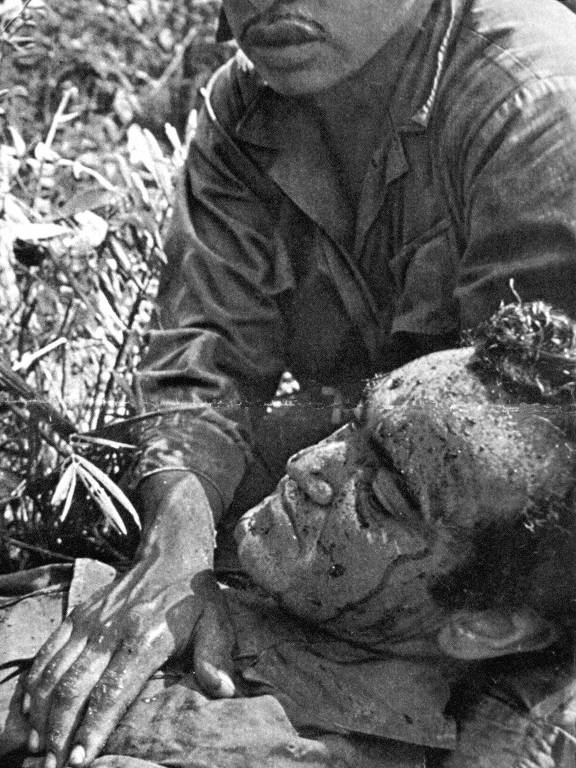 Com manchas de sangue na cabeça, o jornalista José Hamilton Ribeiro é confortado pelo soldado Henry, que coloca a mão em seu peito, após pisar em mina no Vietnã