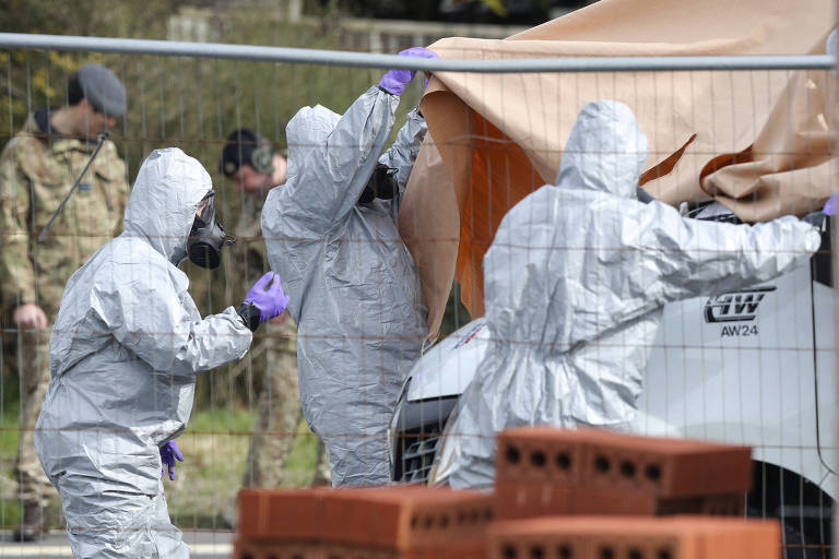Atrás de uma grade de metal, soldados com roupas de proteção contra agentes químicos ou biológicos cobrem camionete com lona durante investigação do envenenamento de Serguei Skripal