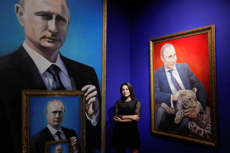 Com vestido preto de mangas transparentes, a estudante Yulia Dyuzheva, 22, posa ao lado de dois quadros representando o presidente Vladimir Putin, um com cachorro e outro com um autorretrato na mão