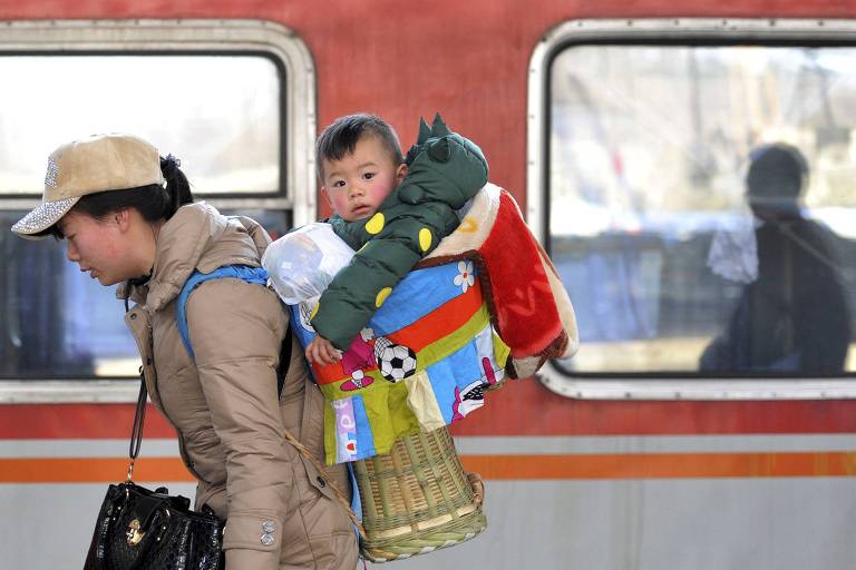 Criança carregada pela mãe em estação de trem na China