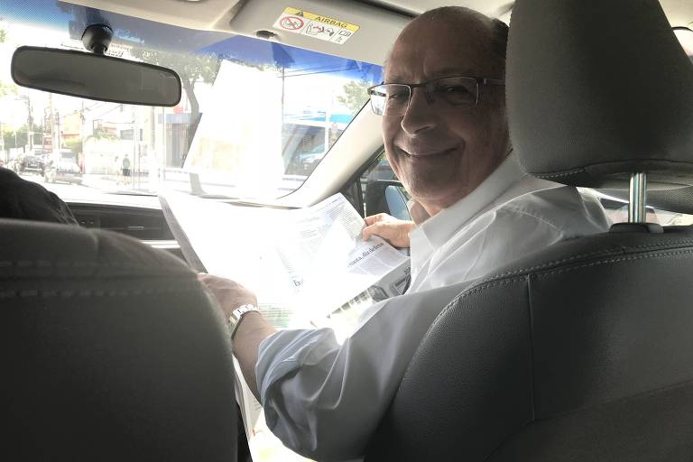 O governador Geraldo Alckmin no carro a caminho de agenda com João Doria e Bruno Covas depois de votar nas prévias do PSDB. Ele segura a Folha no banco do passageiro