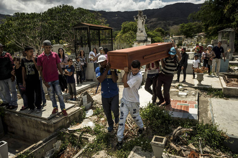 grupo de pessoas carrega caixão em cemitério