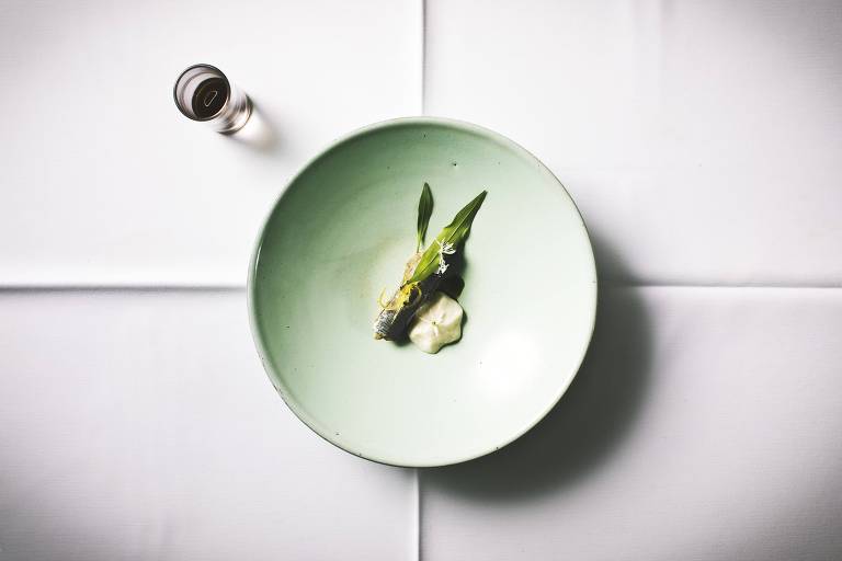 Sardinha e acompanhamentos apresentados em um prato verde claro sobre uma mesa branca