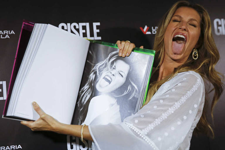 Gisele Bundchen imita seu próprio gesto ao mostrar uma página de seu livro, intitulado Gisele Bundchen, sobre sua carreira de 20 anos de modelo