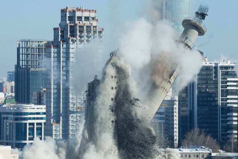Torre de concreto cai após ser implodida, prédios ao fundo