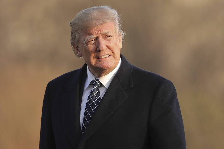 De terno preto, Donald Trump franze o rosto devido ao sol enquanto passa por uma área dos jardins da Casa Branca
