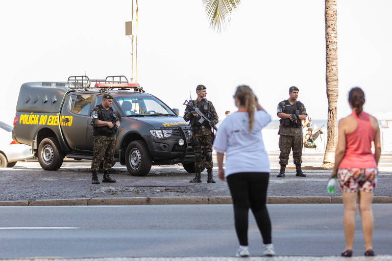 Três policiais do Exército, empunhando armas, fazem patrulha na orla de Copacabana