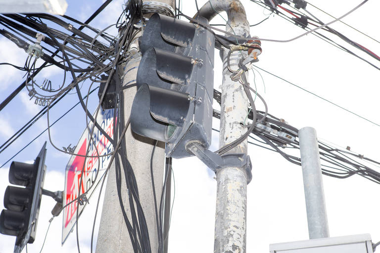 Detalhe de fios emaranhados entre poste de energia e poste semafórico