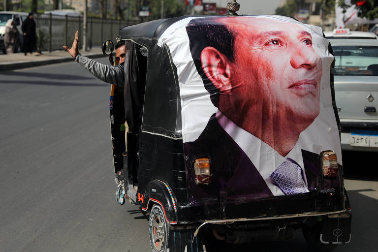 Homem dá tchau ao dar partida com seu triciclo preto que atrás carrega uma foto do líder egípcio, Abdel Fattah al-Sisi em rua do Cairo