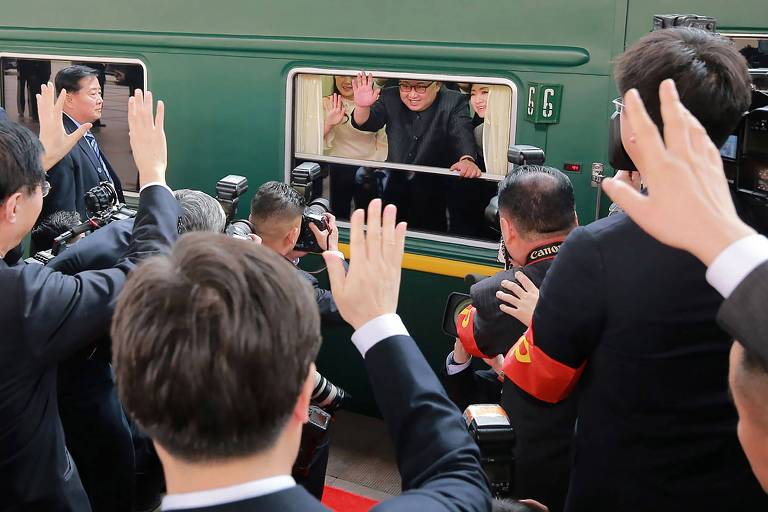 Pessoas acenam ao ditador norte-coreano Kim Jong-un da plataforma enquanto ele responde da janela de um vagão verde de seu trem em Pequim