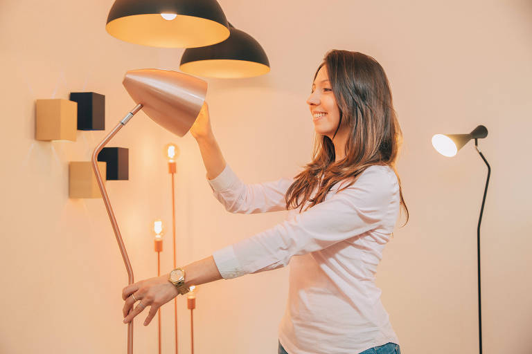 Carolina Garcia, sócia da Munclair Iluminação, na sede da empresa, segura uma das luminárias autorais feitas por eles