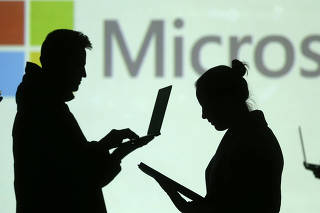 Silhouettes of laptop and mobile device users are seen next to a screen projection of Microsoft logo in this picture illustration