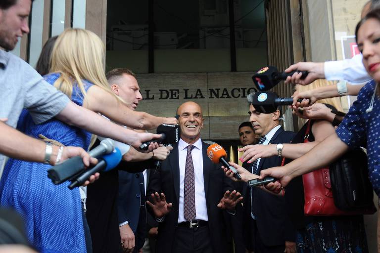 Cercado por repórteres com microfones, Gustavo Arribas sorri ao sair do prédio dos tribunais em Buenos Aires