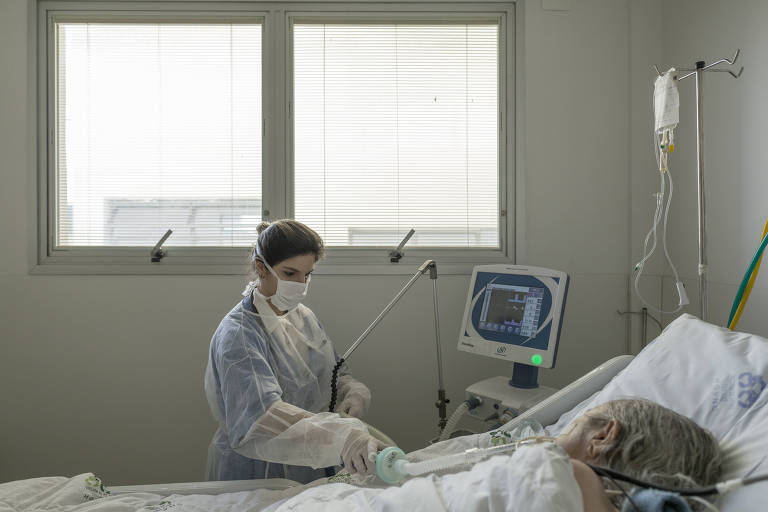 Enfermeira regula equipamento respiratório em UTI de hospital
