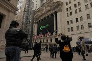 Pedestrians walk past a banner with the Spotify logo on it as the company lists its stock on the New York Stock Exchange with a direct listing in New York