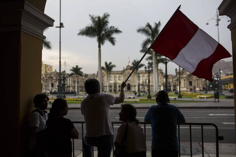 Homem aparece, em meio a outras quatro pessoas agitando a bandeira do Peru na avenida em frente ao palácio presidencial em Lima