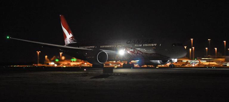 O avião da Qantas Airlines foi fotografado à noite na pista de decolagem. Só é possível vê-lo parcialmente, iluminado pelas luzes externas e da cabine de passageiros