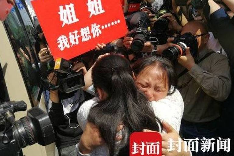 Kang Ying, 27, abraça a mãe em meio a câmeras de vídeo e máquinas fotográficas de jornalistas; acima, um cartaz vermelho de boas-vindas
