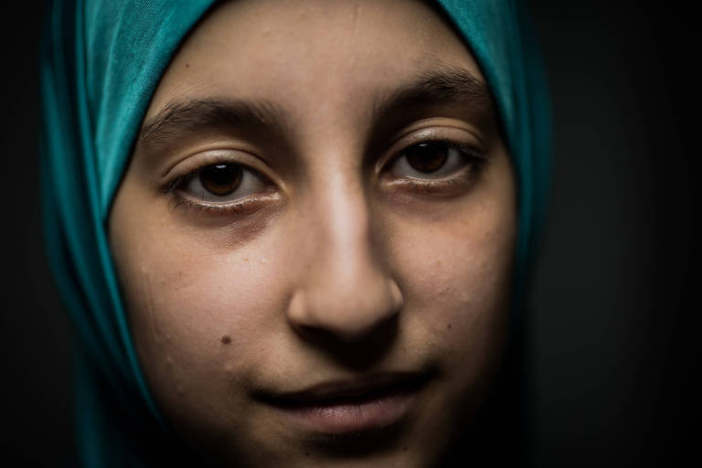 Retrato de menina com lenço azul cobrindo a cabeça, em frente a um fundo cinza