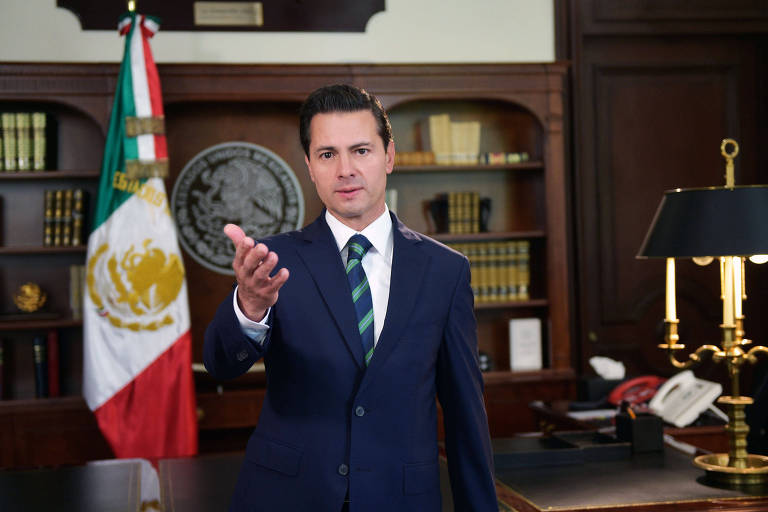 Enrique Peña Nieto estende a mão esquerda enquanto fala aos mexicanos em um vídeo de sua sala; ao fundo, uma bandeira do México e uma estante de livros