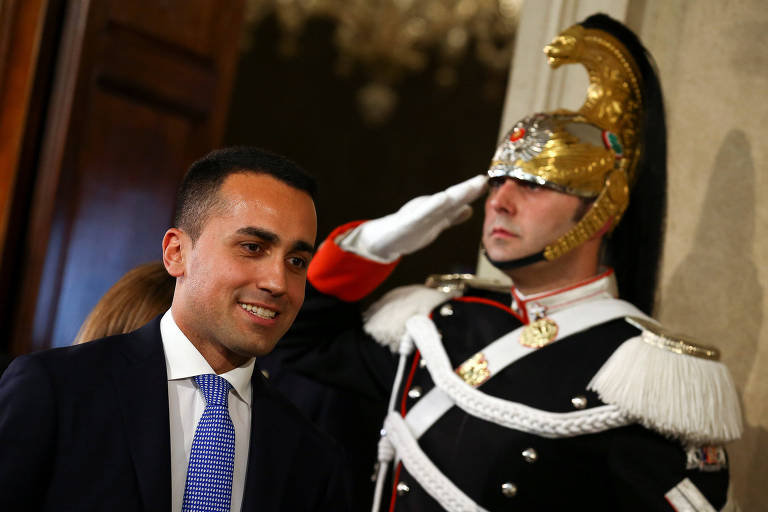 De terno e gravata azul, Luigi Di Maio passa à esquerda de um guarda presidencial italiano que bate continência na porta de um dos salões do palácio