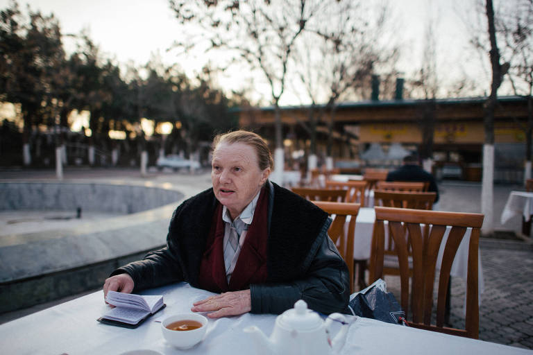 A ativista Yelena Ulaeava aparece na mesa de um café em uma praça de Tashkent, no Uzbequistão; à sua frente, uma xícara de chá, um bloco de papel e um açucareiro